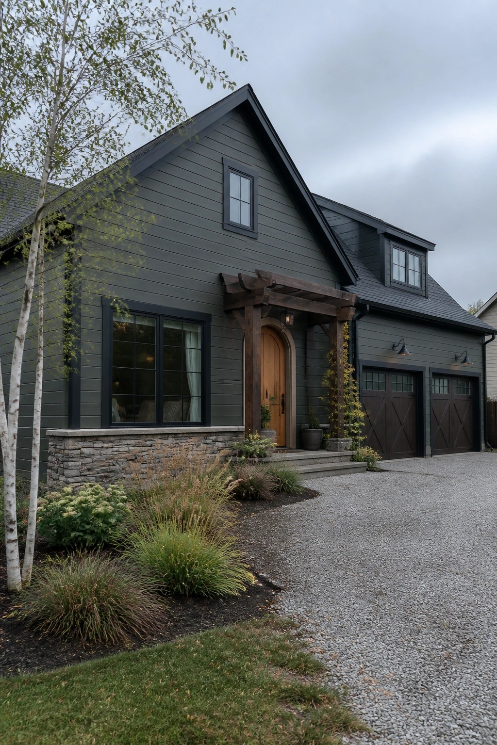 Dark gray modern house with wooden door, pergola, double garage, and gravel drive