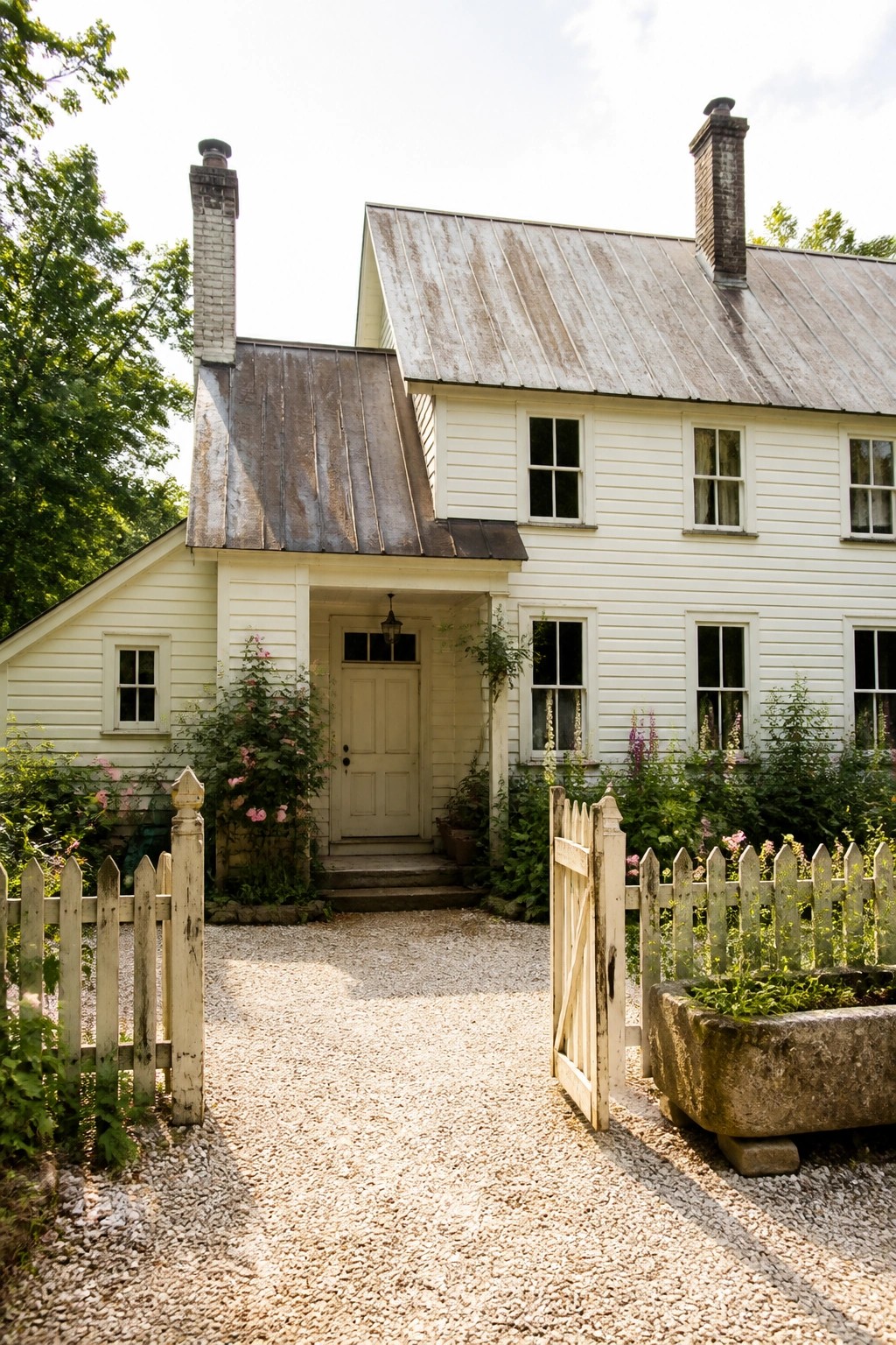 White wooden house with metal roof behind open picket fence on gravel path