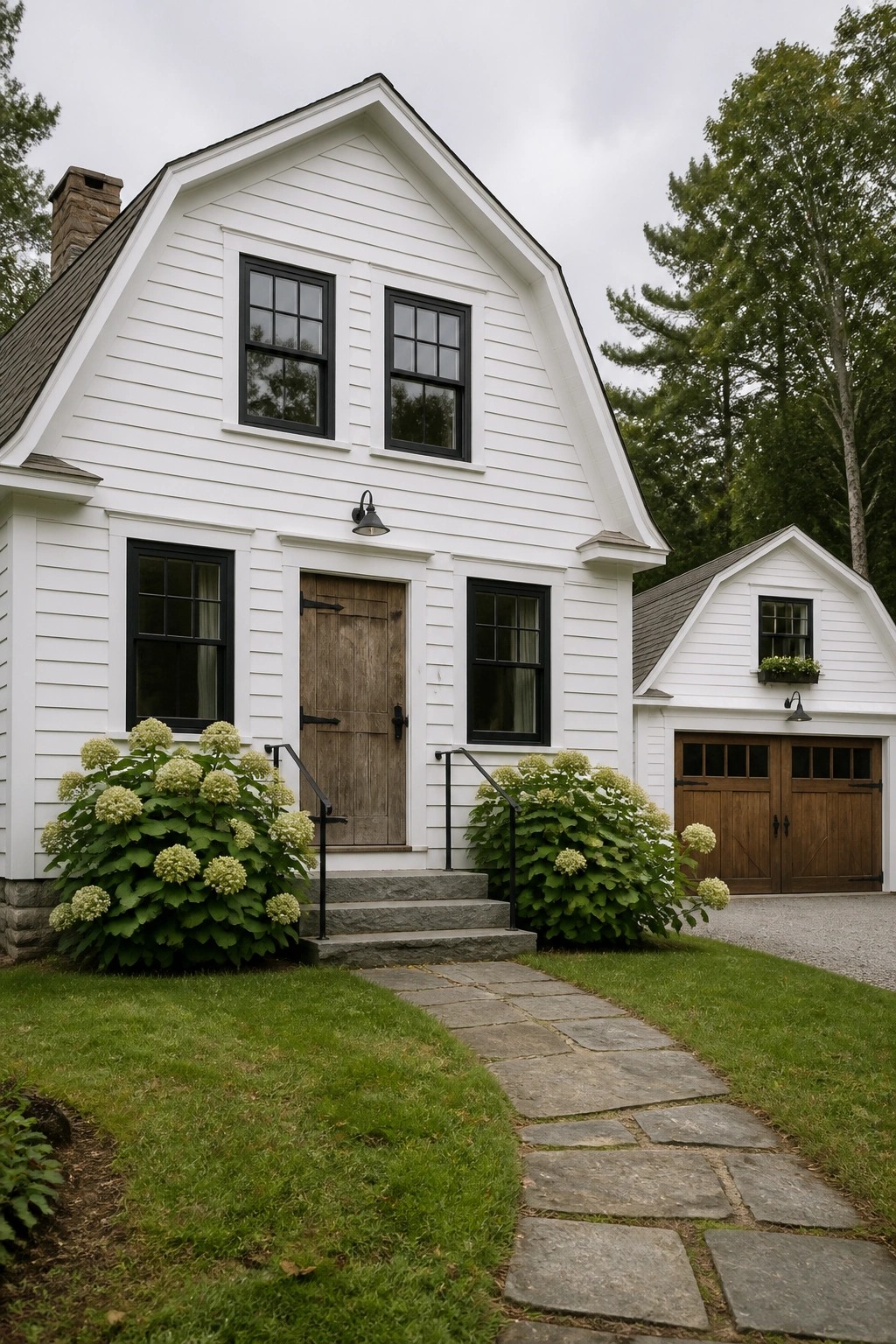 A white gabled farmhouse with black-framed windows, a centered wooden front door, stone steps, and a stone path leading to a matching garage on the right.