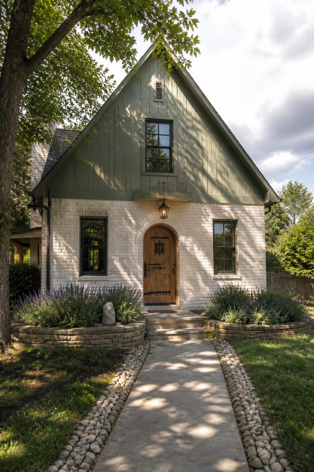 A green gabled house with white brick walls, an arched wooden front door, and a concrete walkway lined with gravel beds.