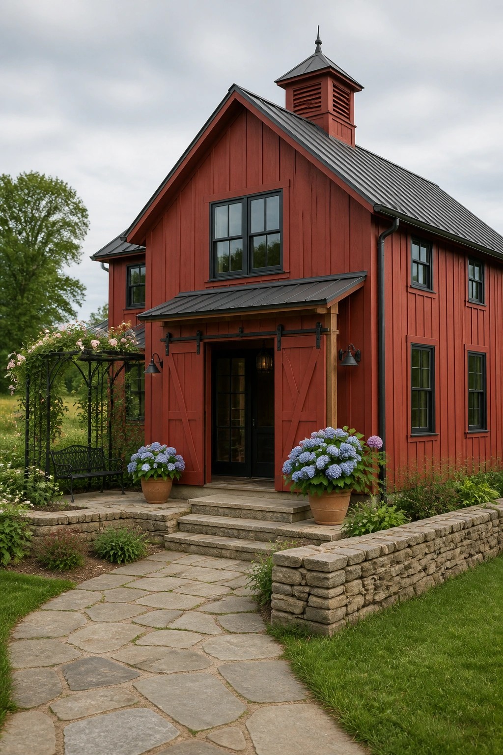A red wooden barn-style house with black windows, a dark metal roof, a cupola, and stone steps leading to the front door.