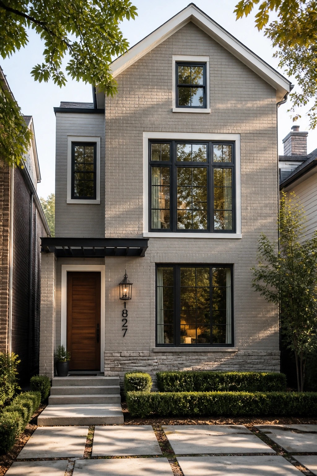 Gray brick two-story house with black-framed windows, wooden door, and stone walkway.