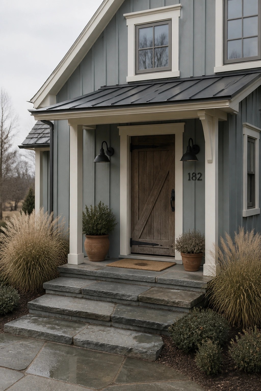 Blue-gray house with wooden door, stone steps, potted plants, and black lanterns.