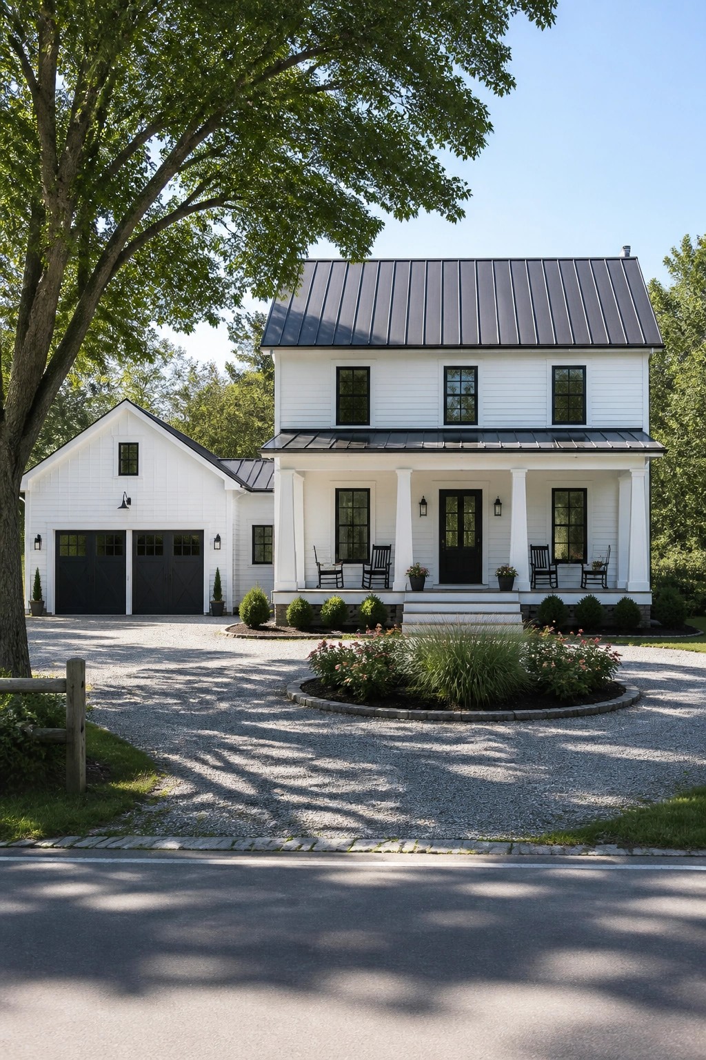 A white two-story farmhouse with a dark metal roof, black-framed windows and doors, a columned front porch, and an attached garage, viewed from a gravel driveway.
