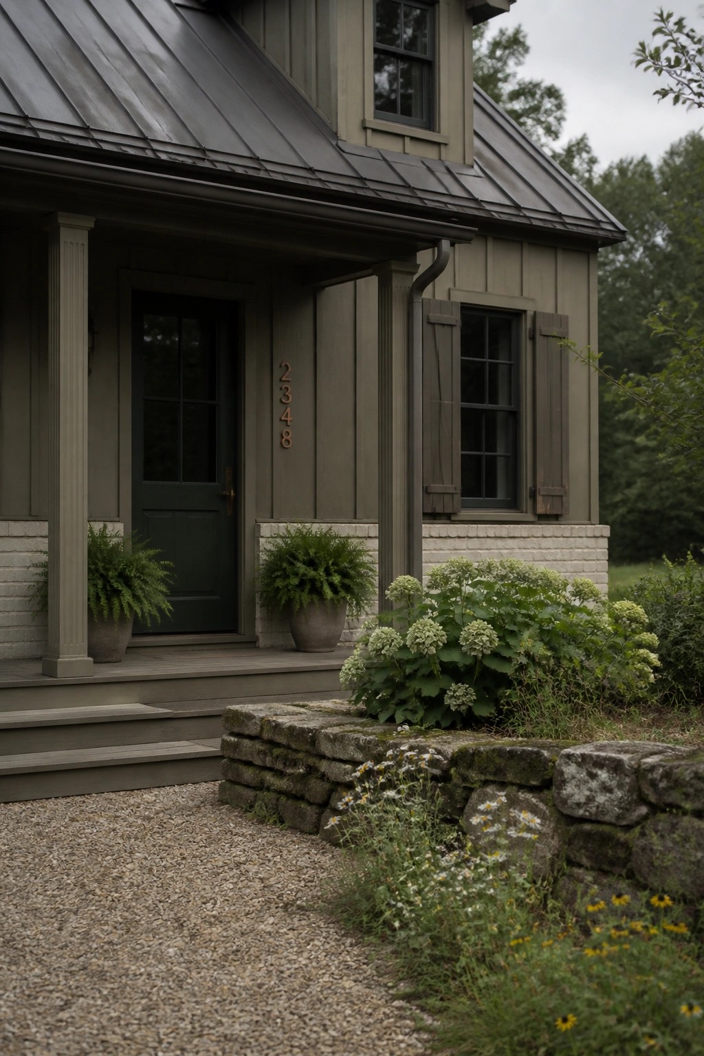 A farmhouse exterior with muted sage green siding next to a stone foundation.