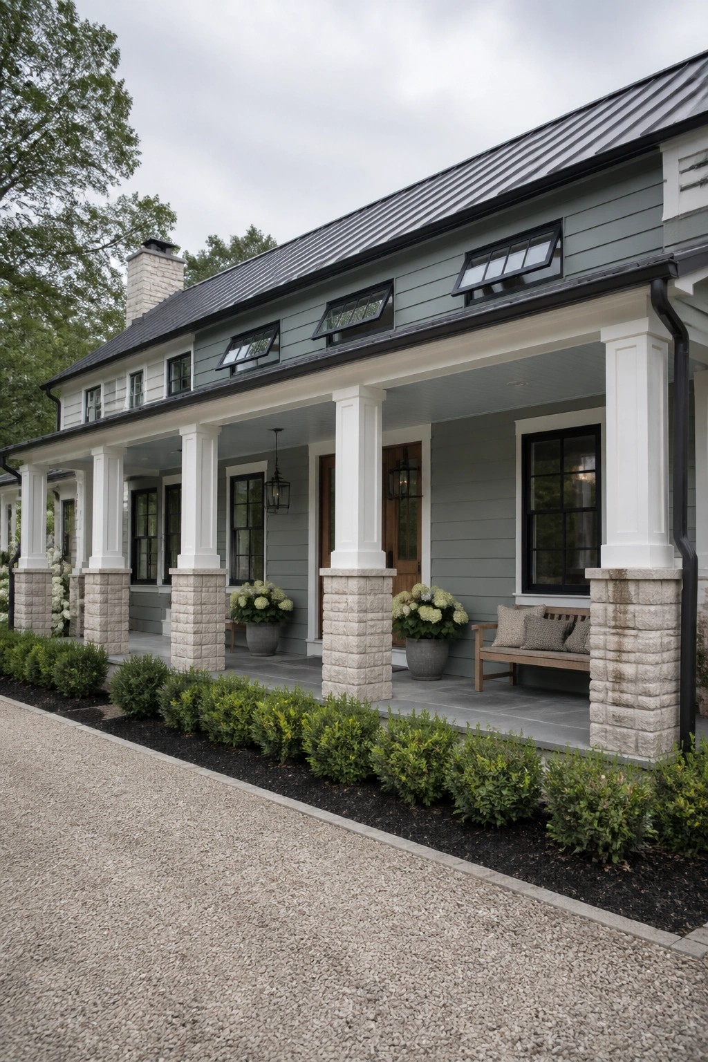 The house exterior shows muted sage green siding with white porch columns and a dark metal roof.