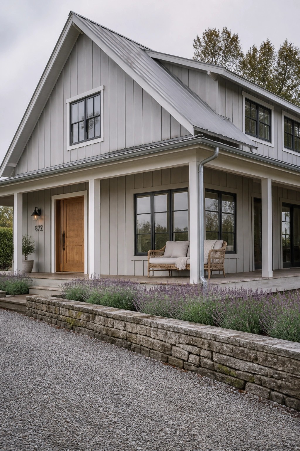 Gray farmhouse with metal roof, porch seating, lavender garden, and stone wall