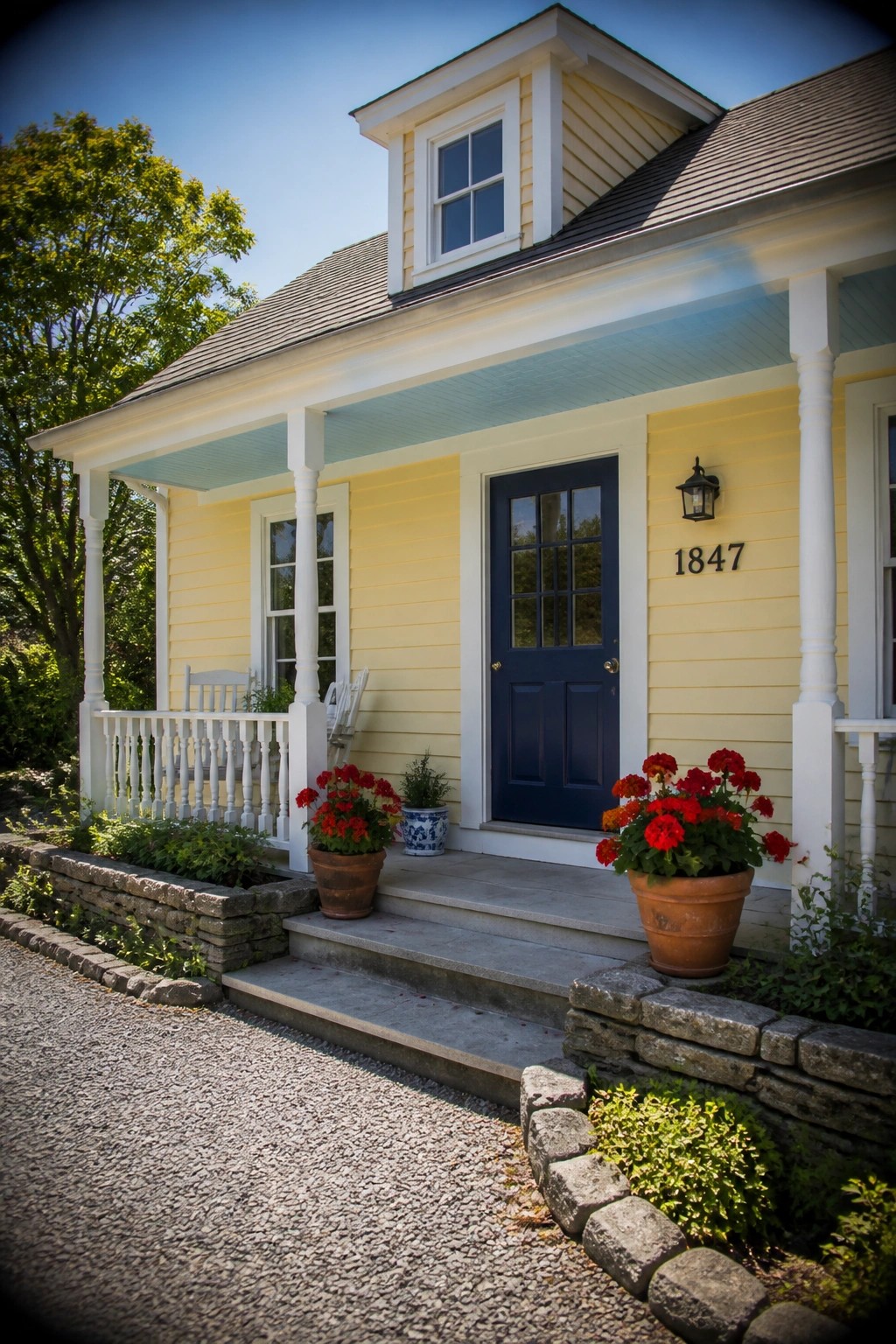 Yellow house with blue door, white porch, red flowers in pots on steps