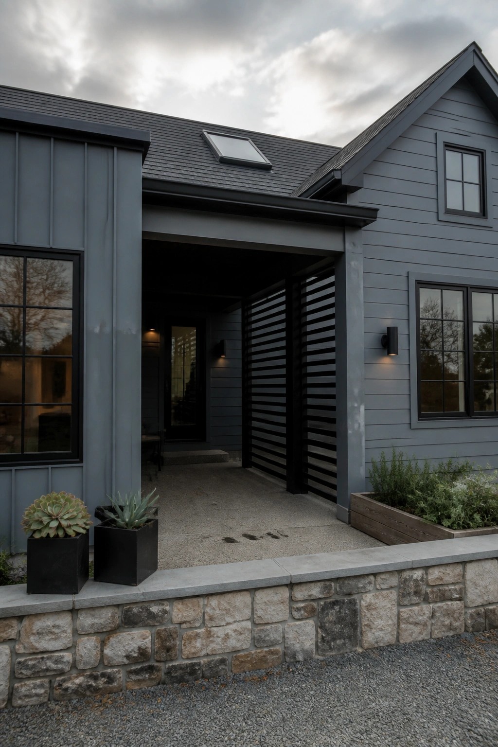 Modern gray house with stone wall, potted succulents, and covered slatted entryway