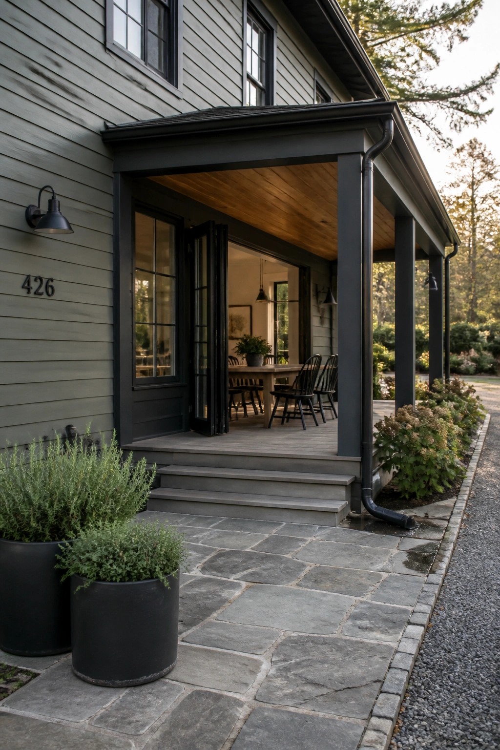 Gray house with open black doors, covered porch, stone steps and potted plants