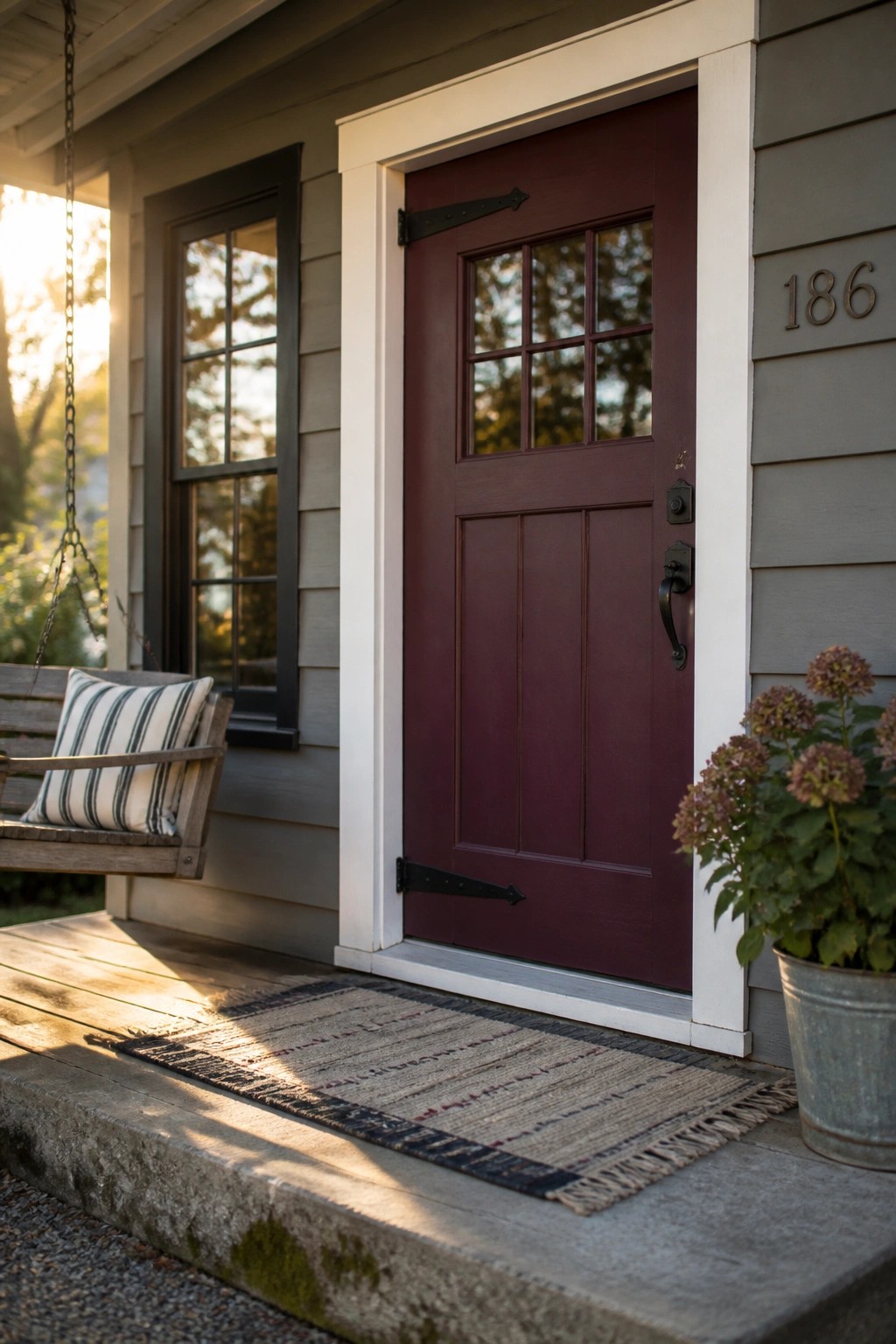 A deep burgundy front door on a gray farmhouse with white trim.