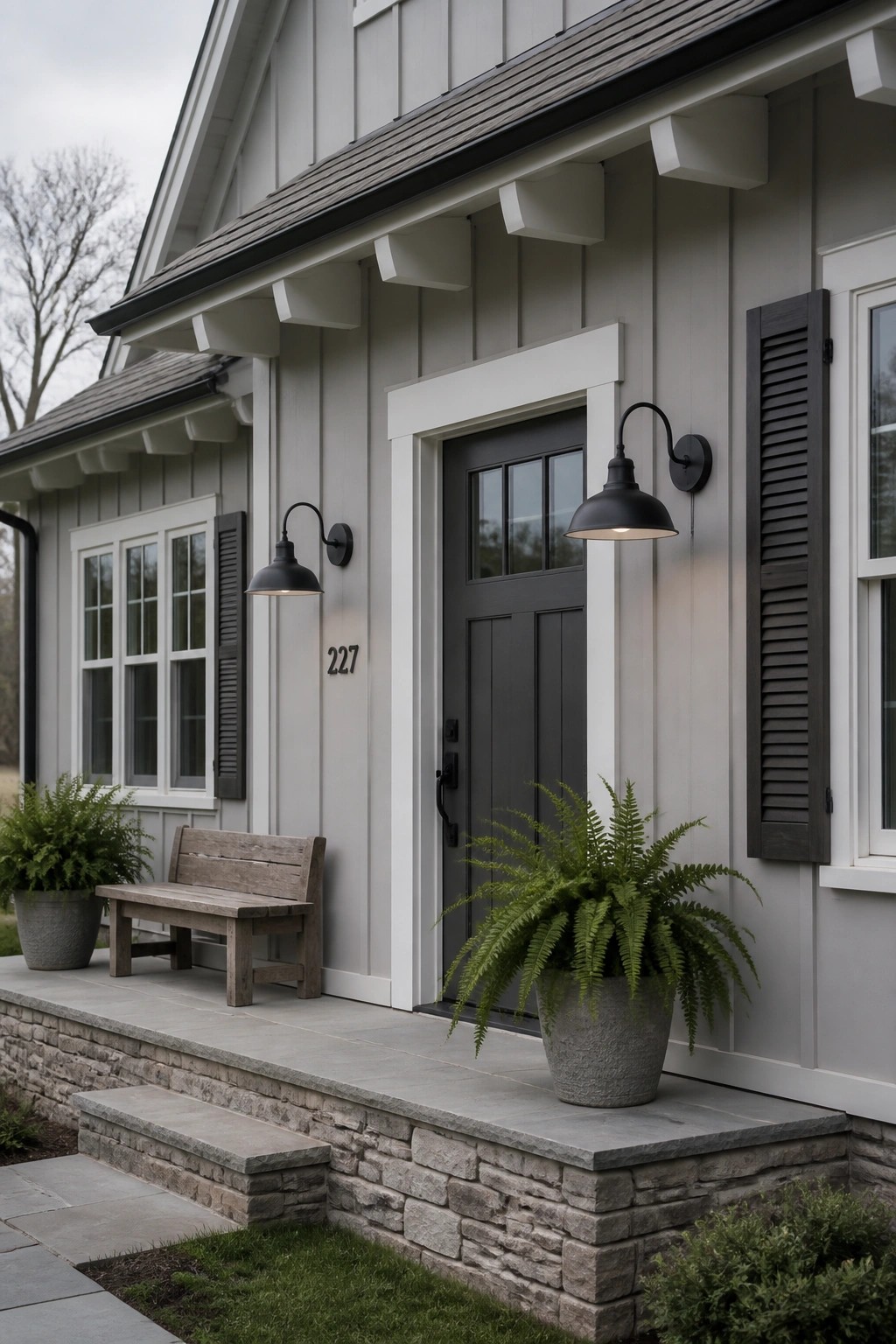 Gray house entrance with black door, sconce lights, bench, and potted ferns.