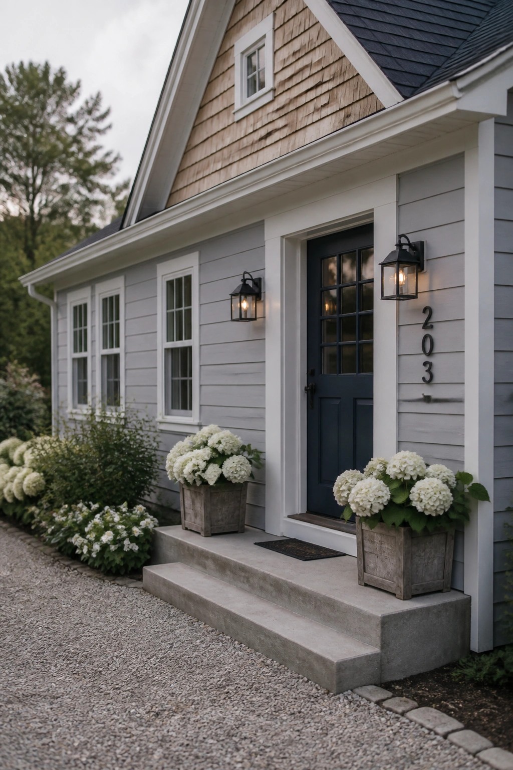 Gray house with blue door, white hydrangeas in planters on concrete steps.