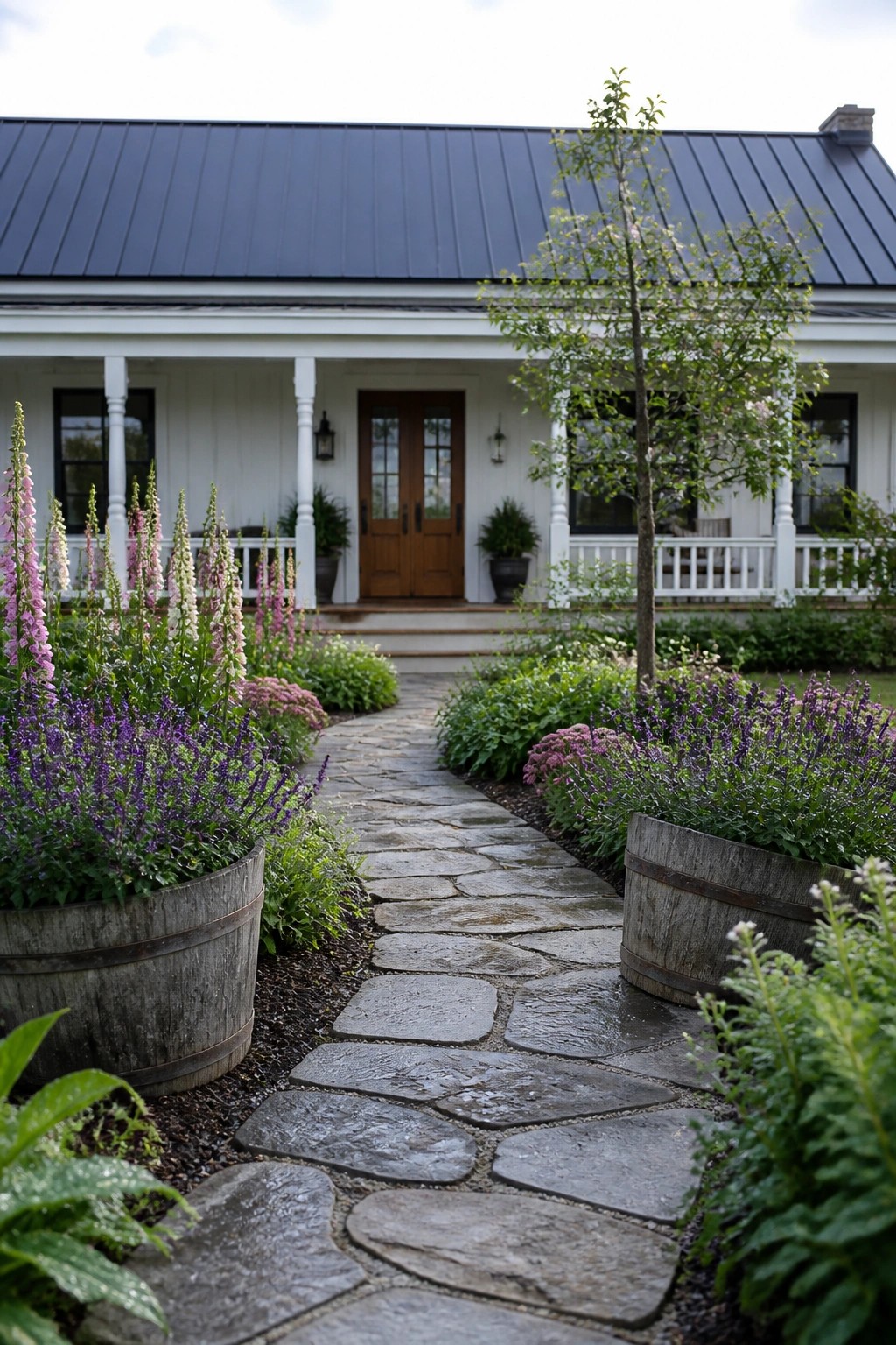 Stone path through blooming gardens to white farmhouse porch with barrels.
