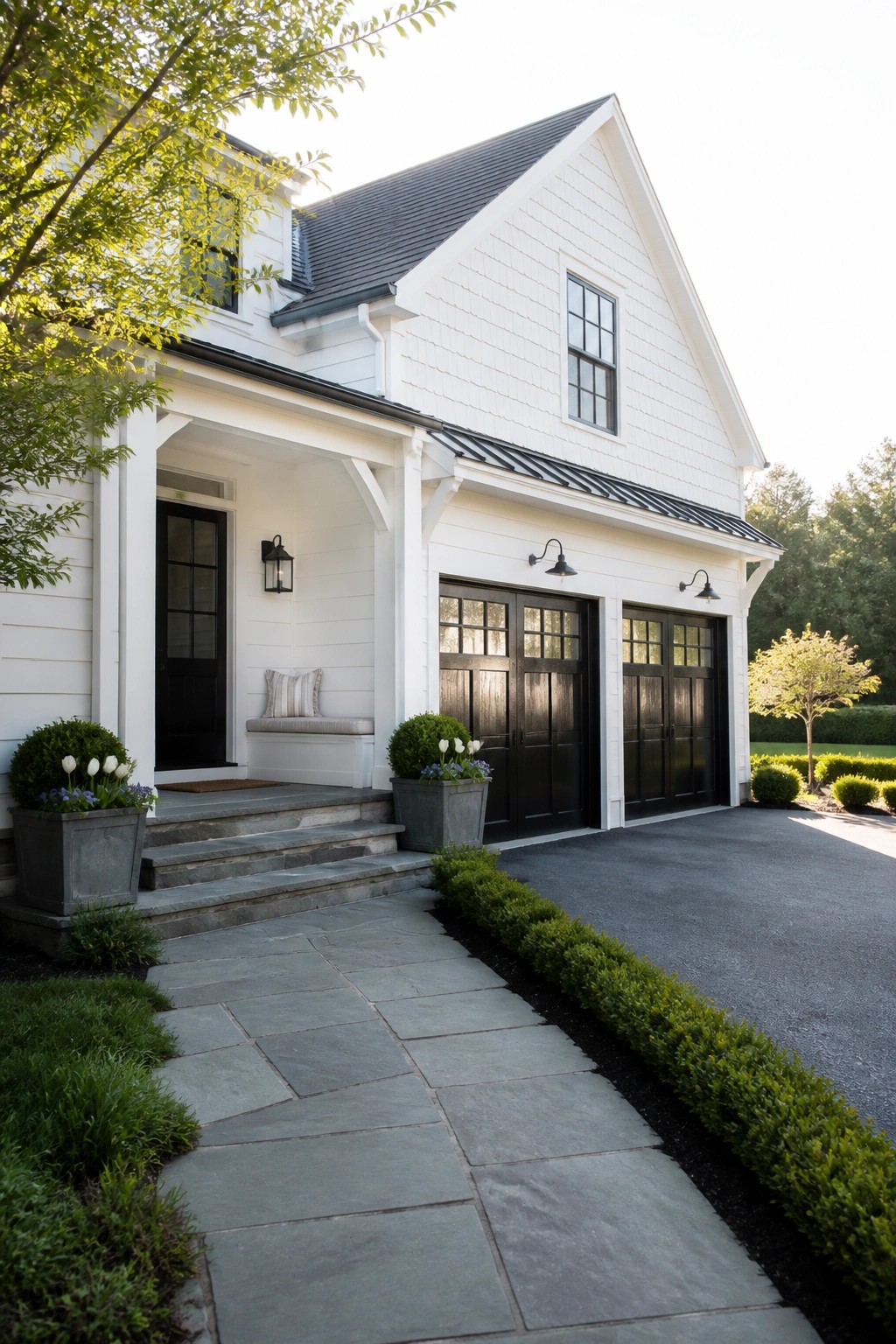 White farmhouse exterior with black front door, black garage doors, stone steps, and paved walkway.