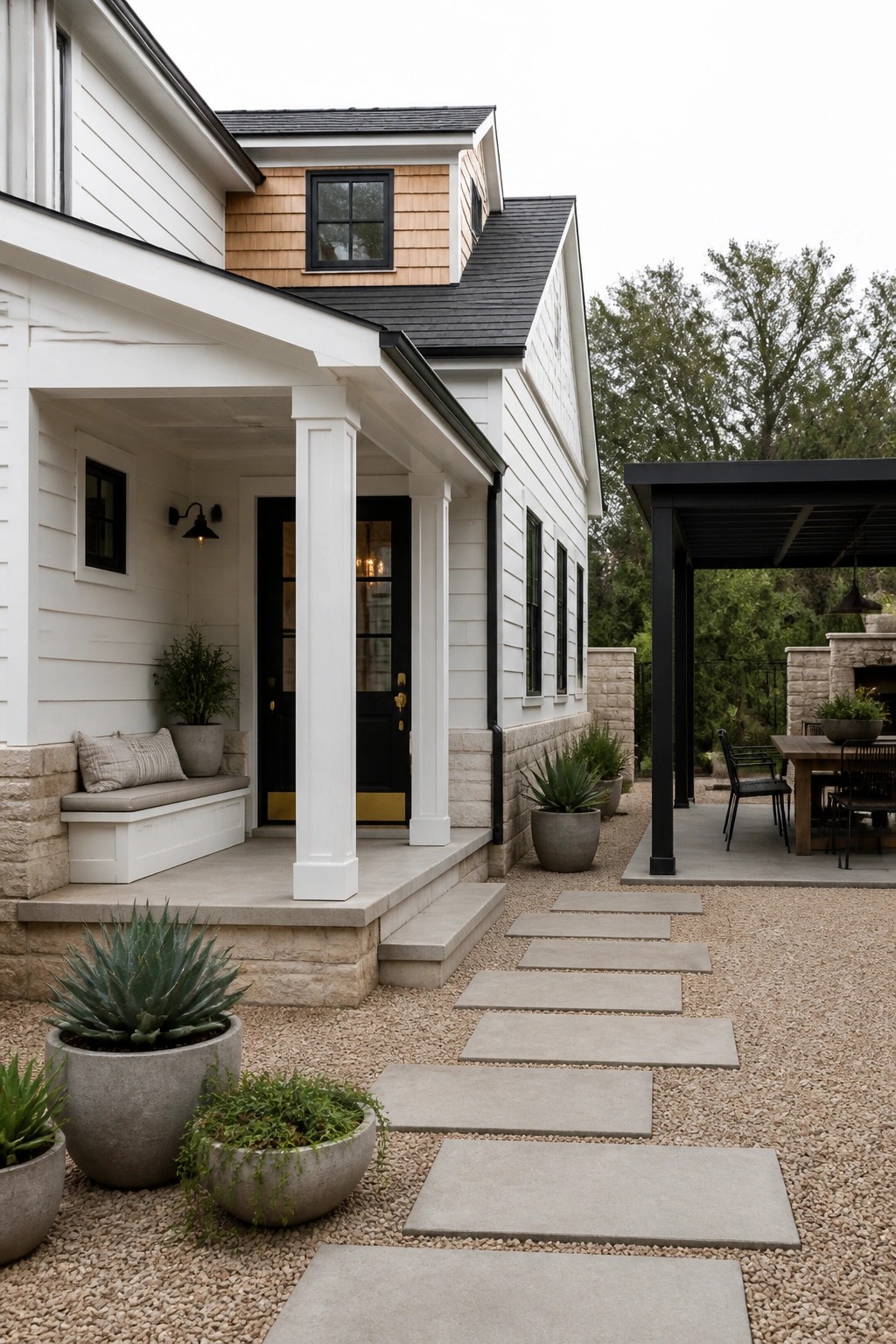 A white farmhouse exterior with a black front door, white porch columns, stone foundation, and a gravel path with concrete pavers leading to the steps.