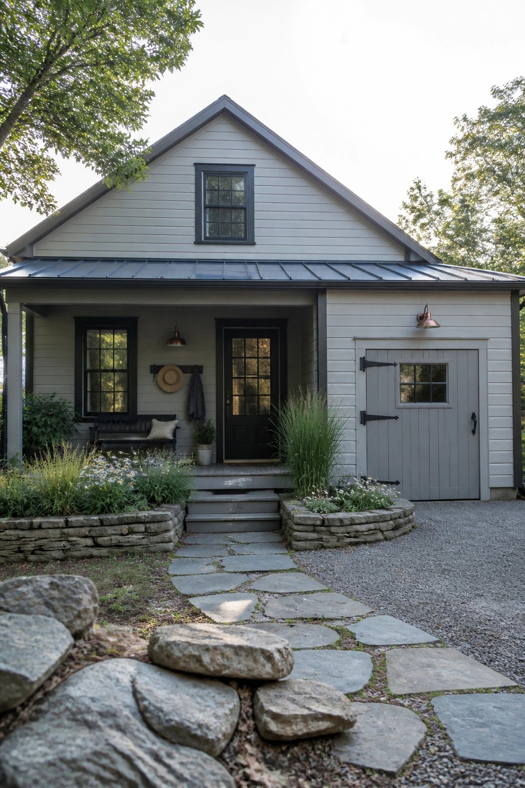 A light gray gabled house with black window and door trim, a dark metal roof, gray steps, and a stone path leading to the front door.