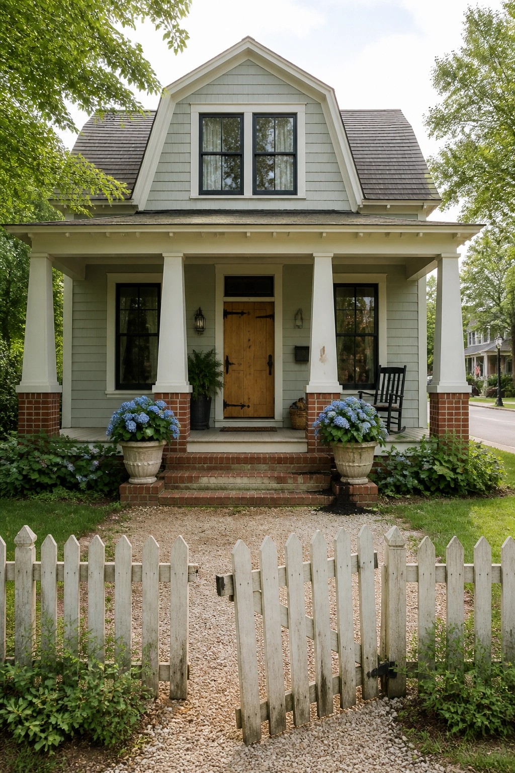 Light blue house with white porch, potted blue flowers, and open picket fence gate.
