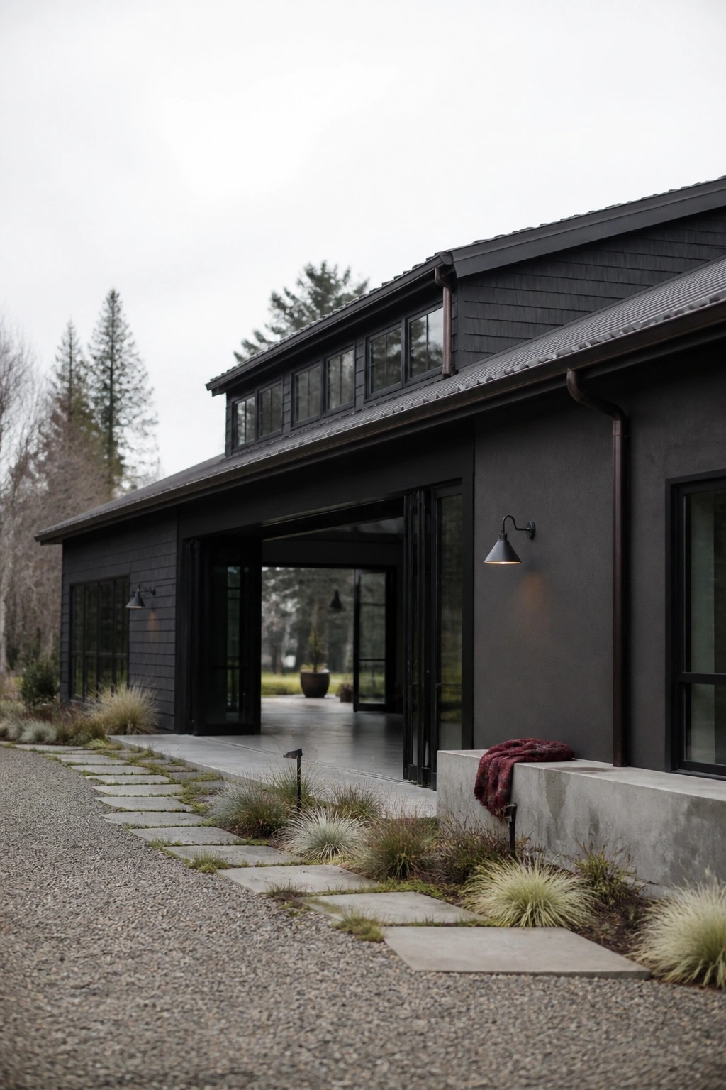 A dark gray modern farmhouse exterior with black trim, large open barn-style doors, and a stone pathway leading to the entrance.
