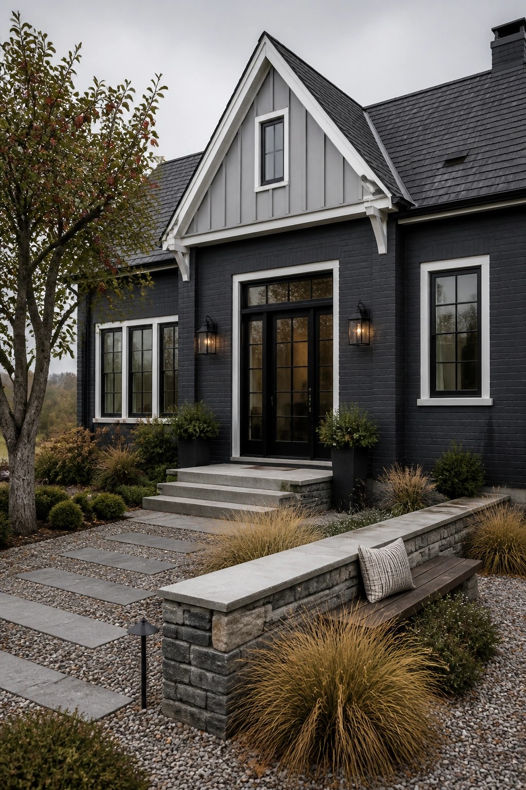 A dark painted brick farmhouse with white trim, black doors and windows, concrete steps, and a stone bench in the front yard.