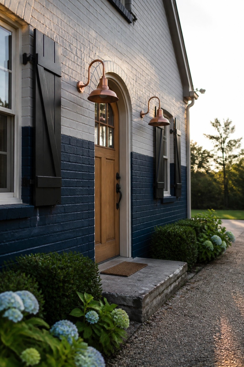 White brick house with blue accents, arched door, copper lights, and hydrangeas.