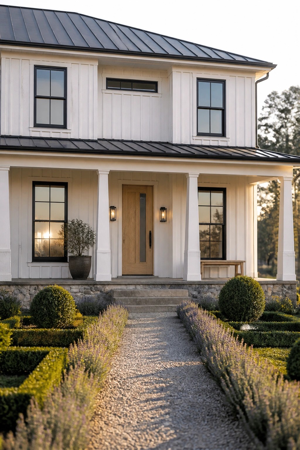 A two-story white farmhouse exterior with a black metal roof, black-framed windows arranged symmetrically around a central wooden door, white porch columns, and a gravel path leading to stone steps.