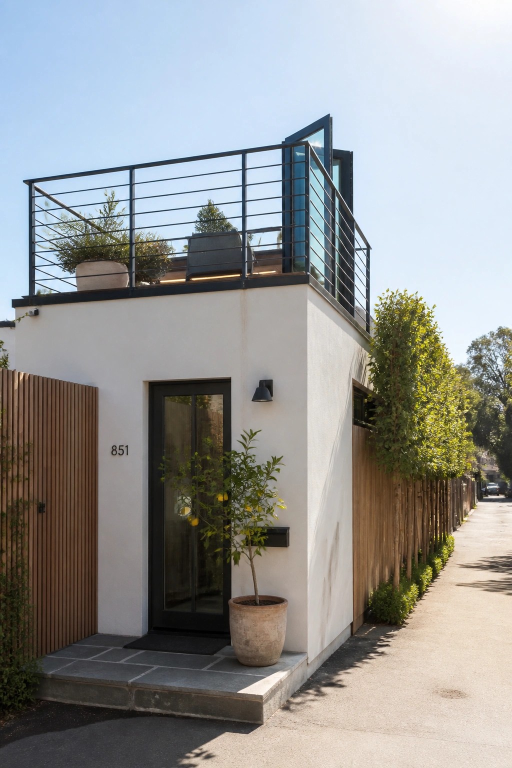 A small white house with a black door and a rooftop terrace enclosed by a black metal railing.