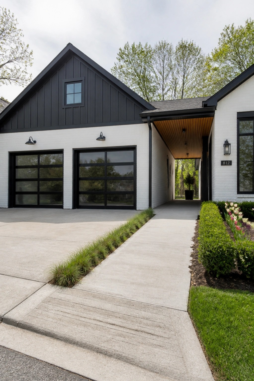 A white brick house exterior with black trim, two large black garage doors, a gabled roof section with vertical siding, and a concrete driveway leading to a covered entry.