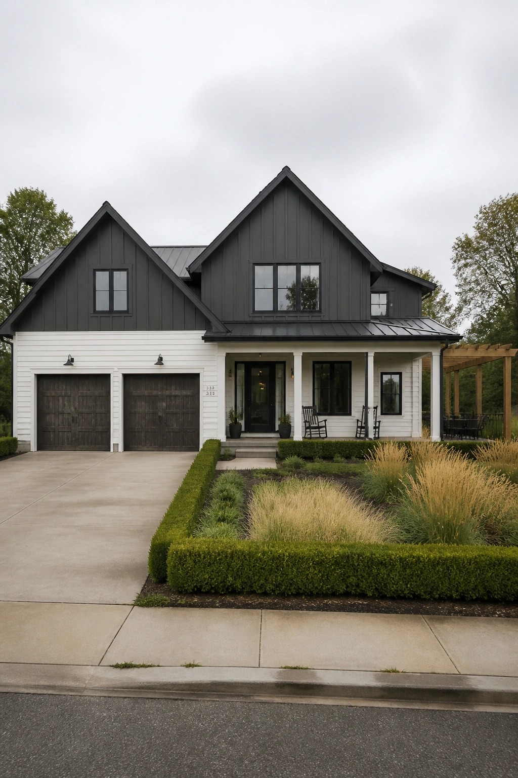 A two-story modern farmhouse with dark board and batten siding on the upper gables and white siding on the lower level, including two dark garage doors and a covered front porch.