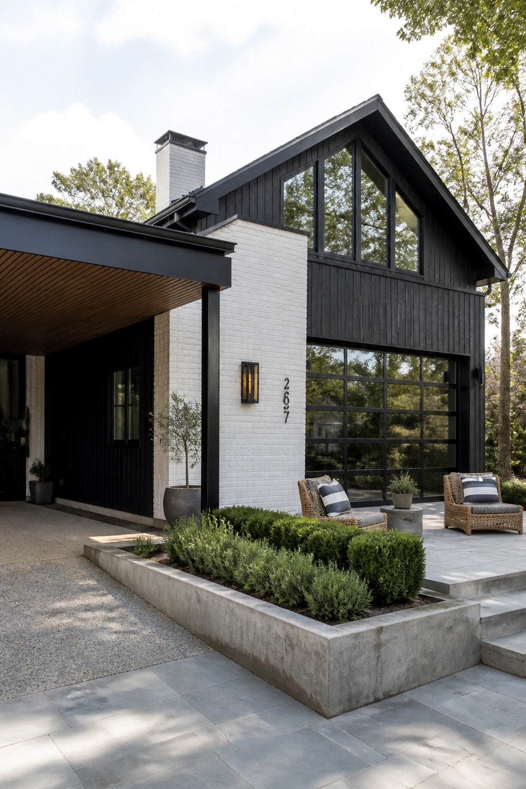 A contemporary farmhouse exterior featuring white brick, black siding, a dark gabled roof, large black-framed windows, and a concrete planter with shrubs in the foreground.