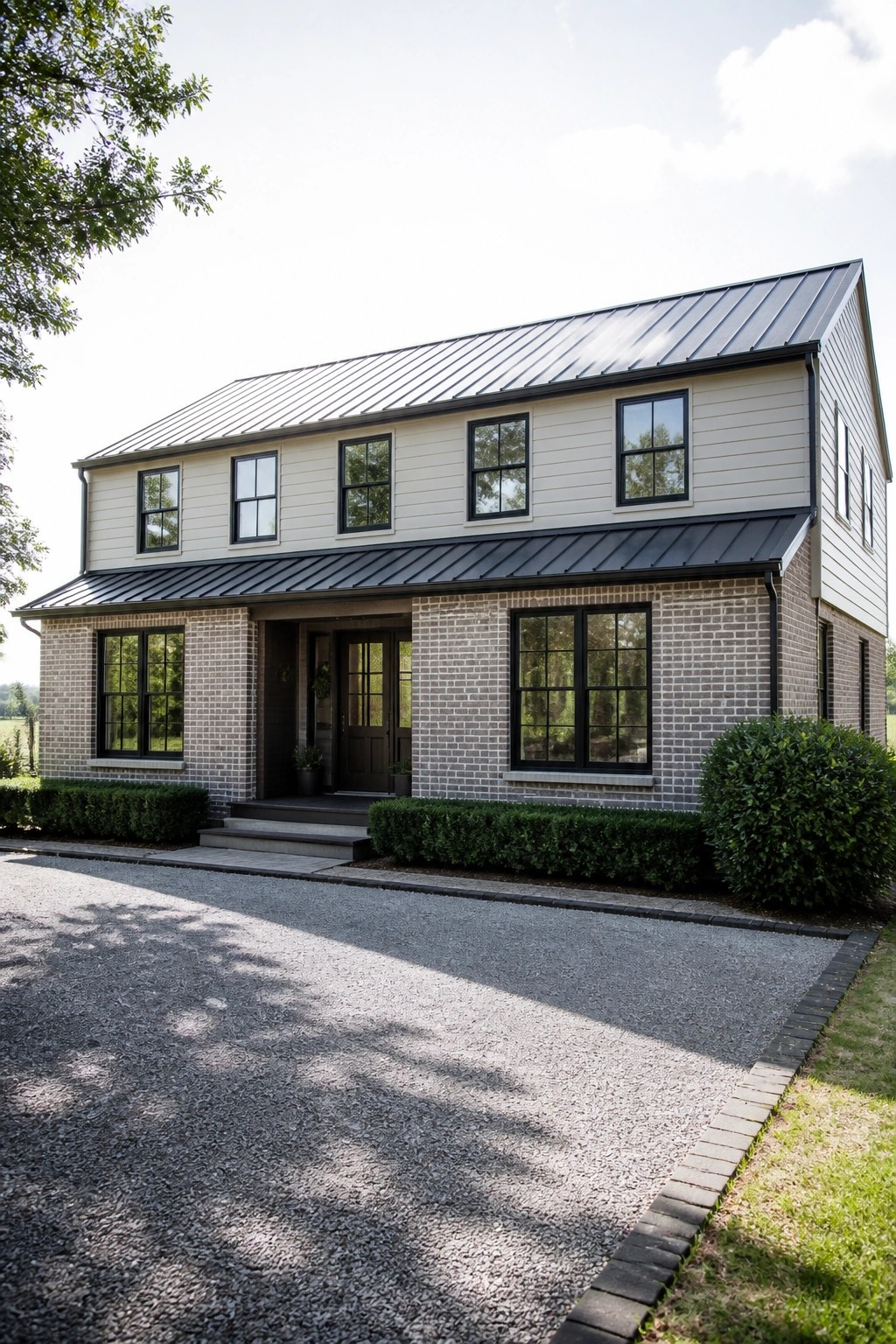 A two-story farmhouse with gray brick on the lower level, light siding above, a black metal roof, and black-framed windows.