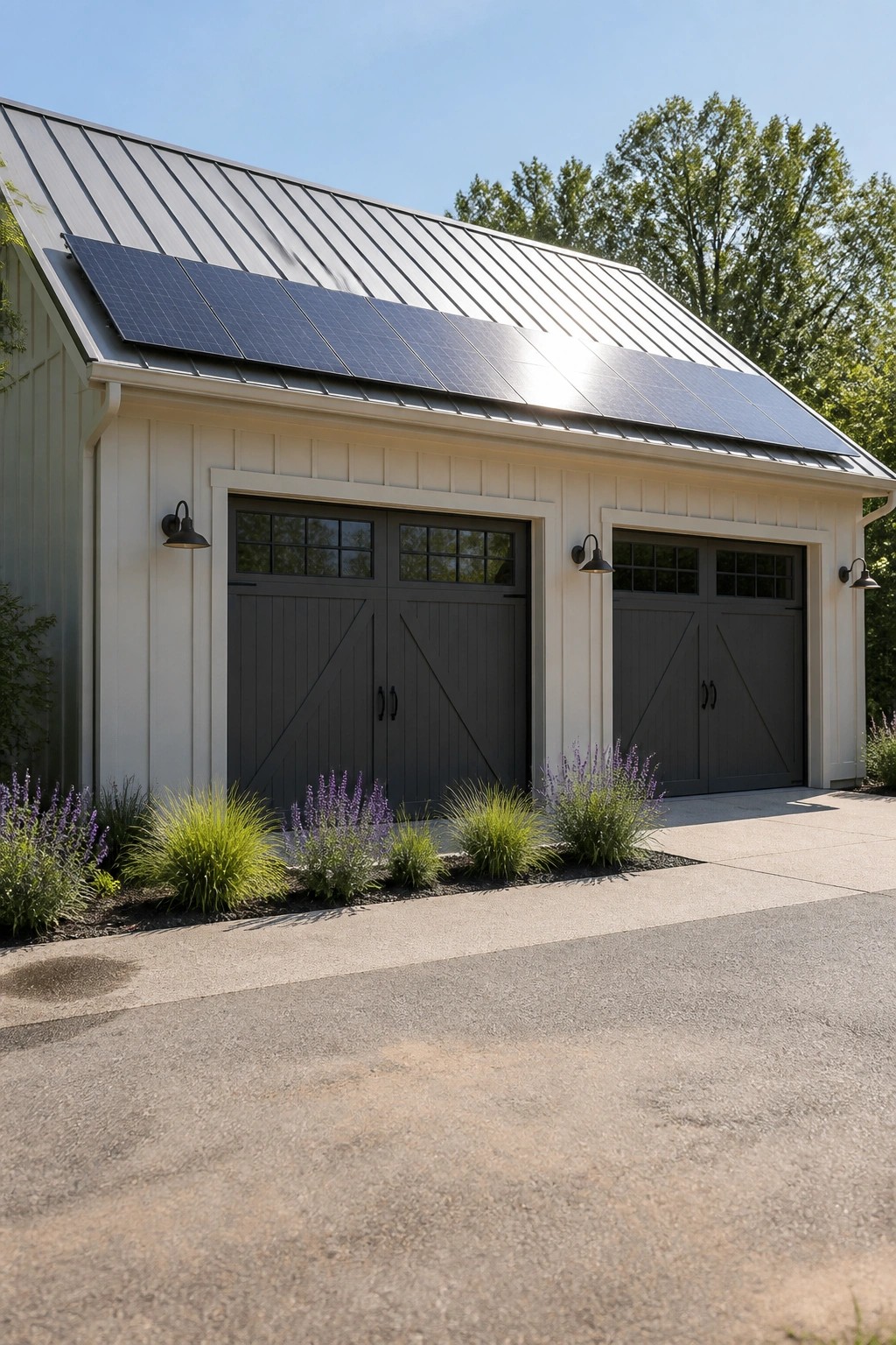 A light-colored farmhouse-style garage with dark gray barn doors, solar panels on a metal roof, and landscaping along the front.