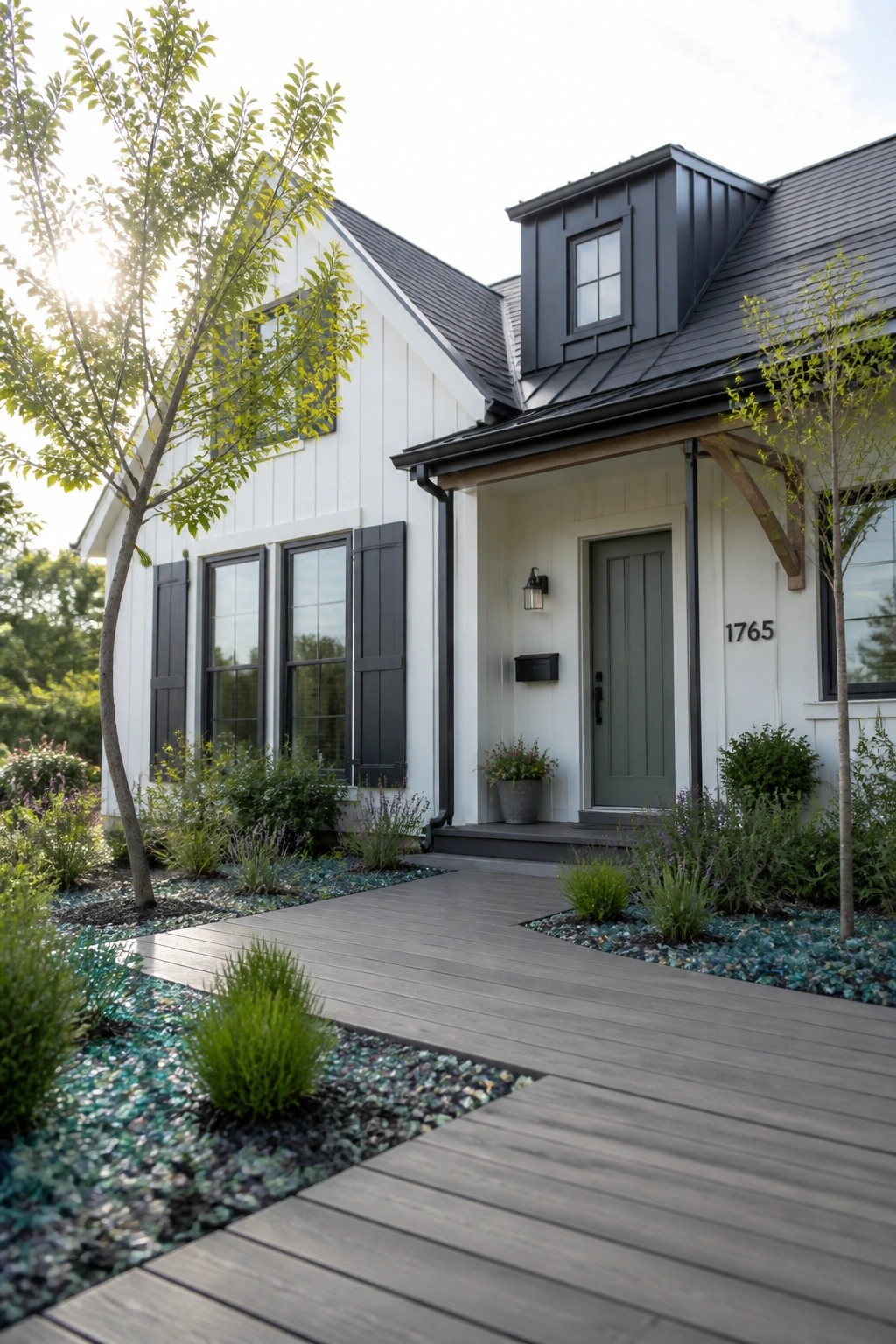A white farmhouse exterior with dark metal roofing, black shutters, and a green front door, seen from a wooden walkway lined with gravel and plants.