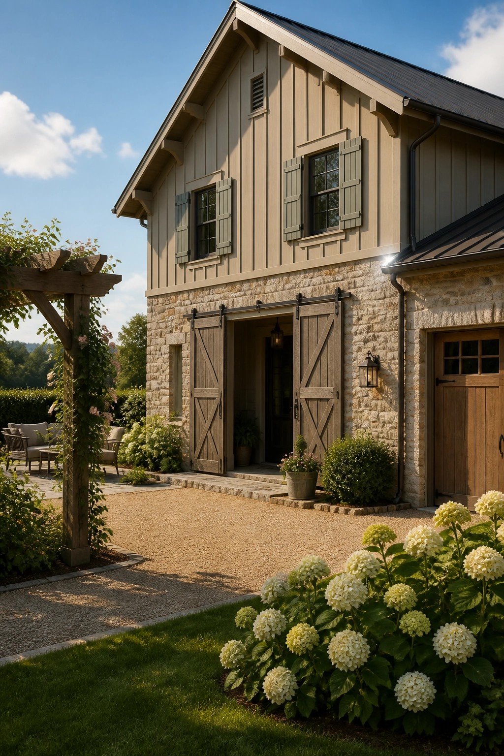 A two-story farmhouse exterior with beige wood siding, a stone base, and large wooden sliding barn doors at the main entrance, with white hydrangeas in the foreground.