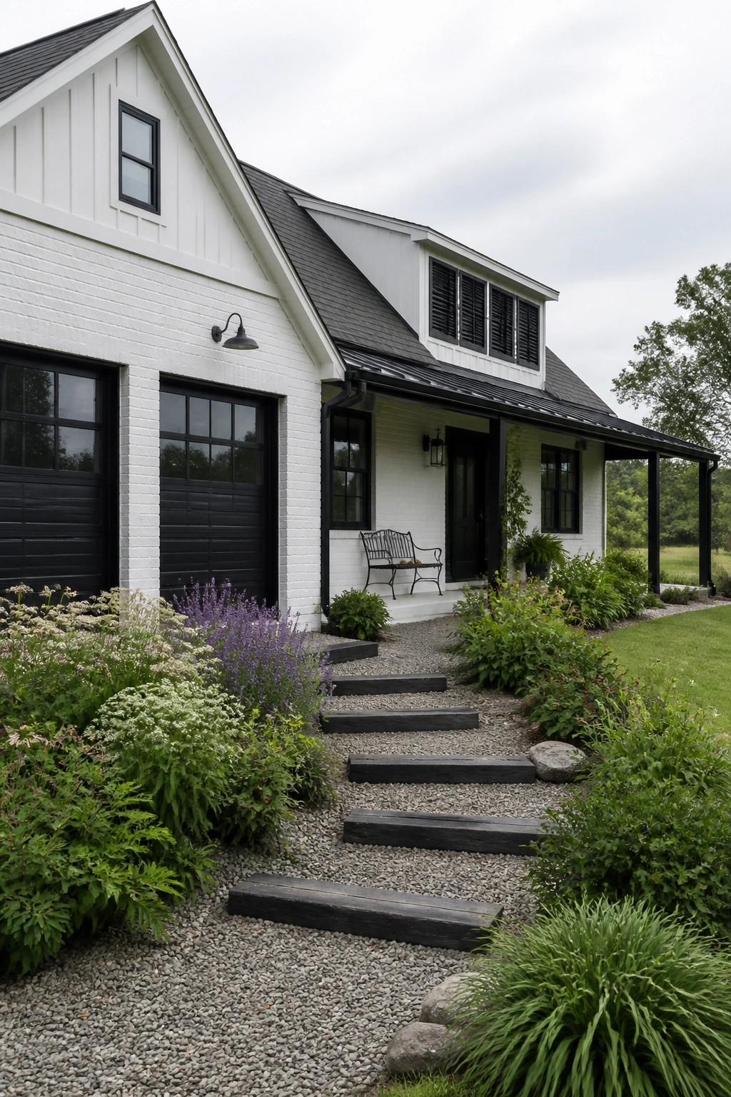 A white brick farmhouse exterior with black garage doors, black windows, black door, and black trim, set against a gravel path and garden beds.