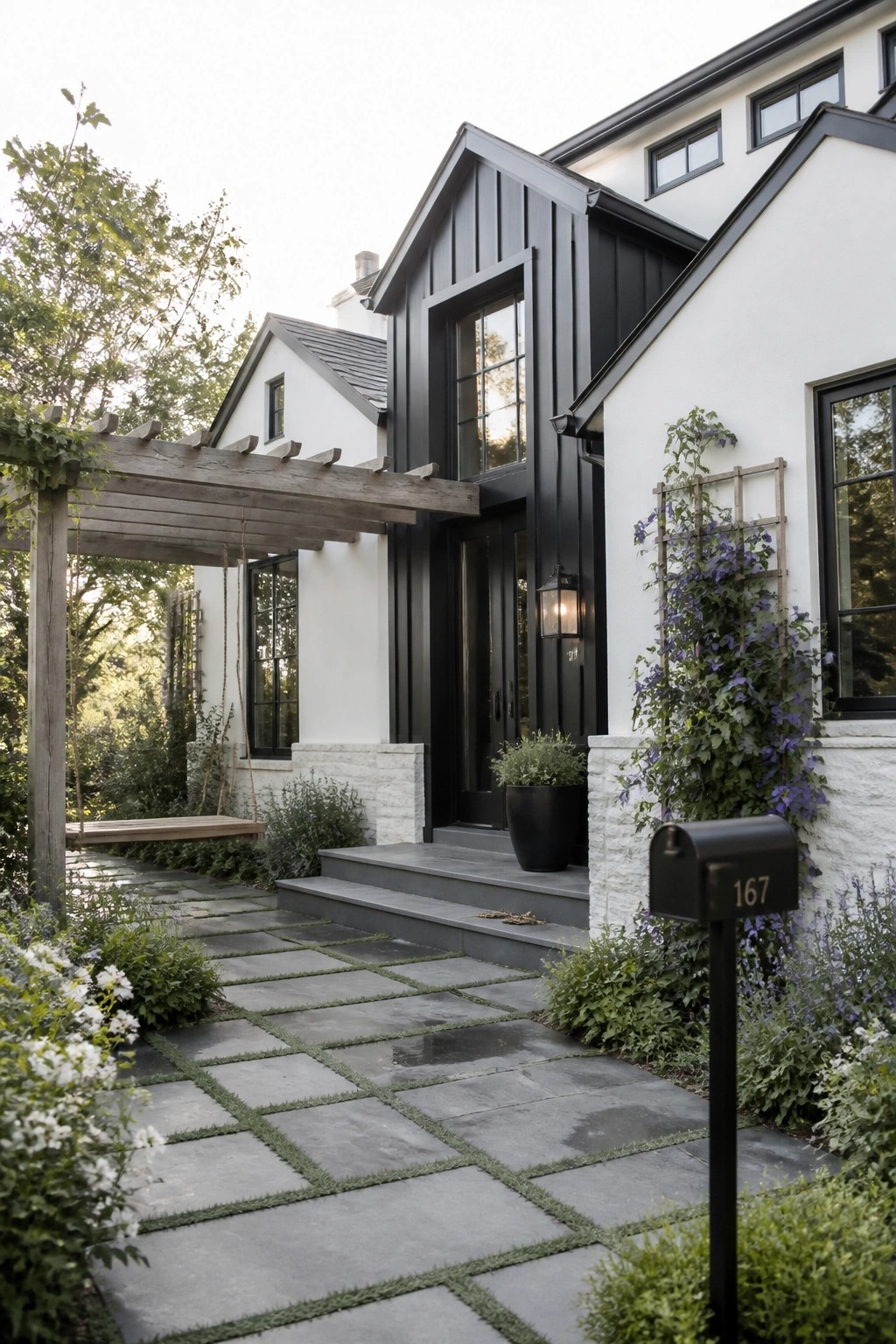 A white farmhouse exterior with black trim, black windows, and a black front door, shown with a stone pathway, steps, and garden plantings in the foreground.