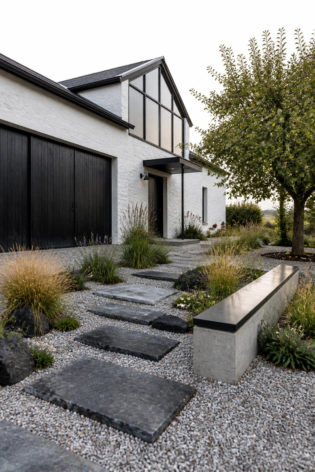 A white stucco farmhouse with black garage doors, window frames, and entry door, shown with a gravel path of large stepping stones and low plantings along the front.