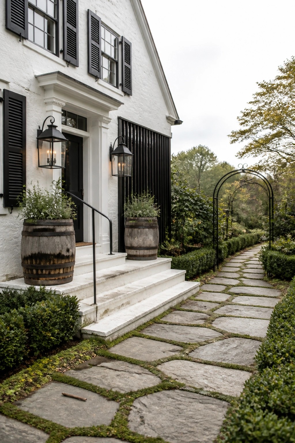 A white farmhouse with black shutters, black door, and two wooden barrel planters beside the front steps, with a stone path leading to the entrance.