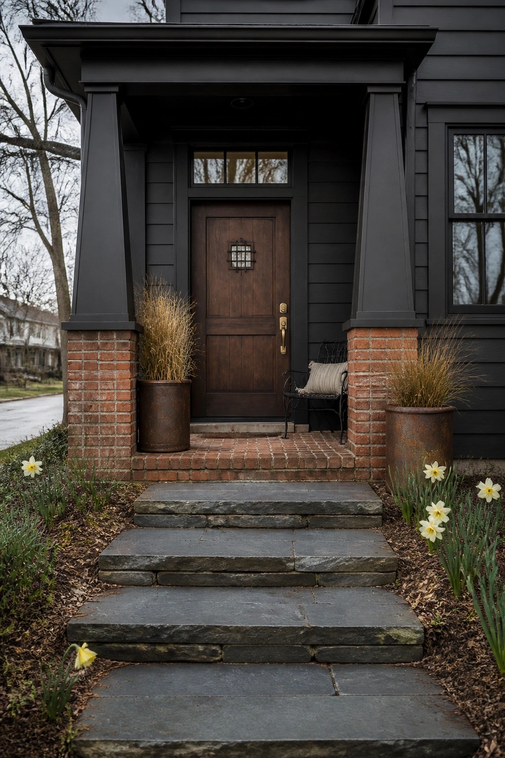 Dark house with wooden door, brick pillars, stone steps, and yellow daffodils.