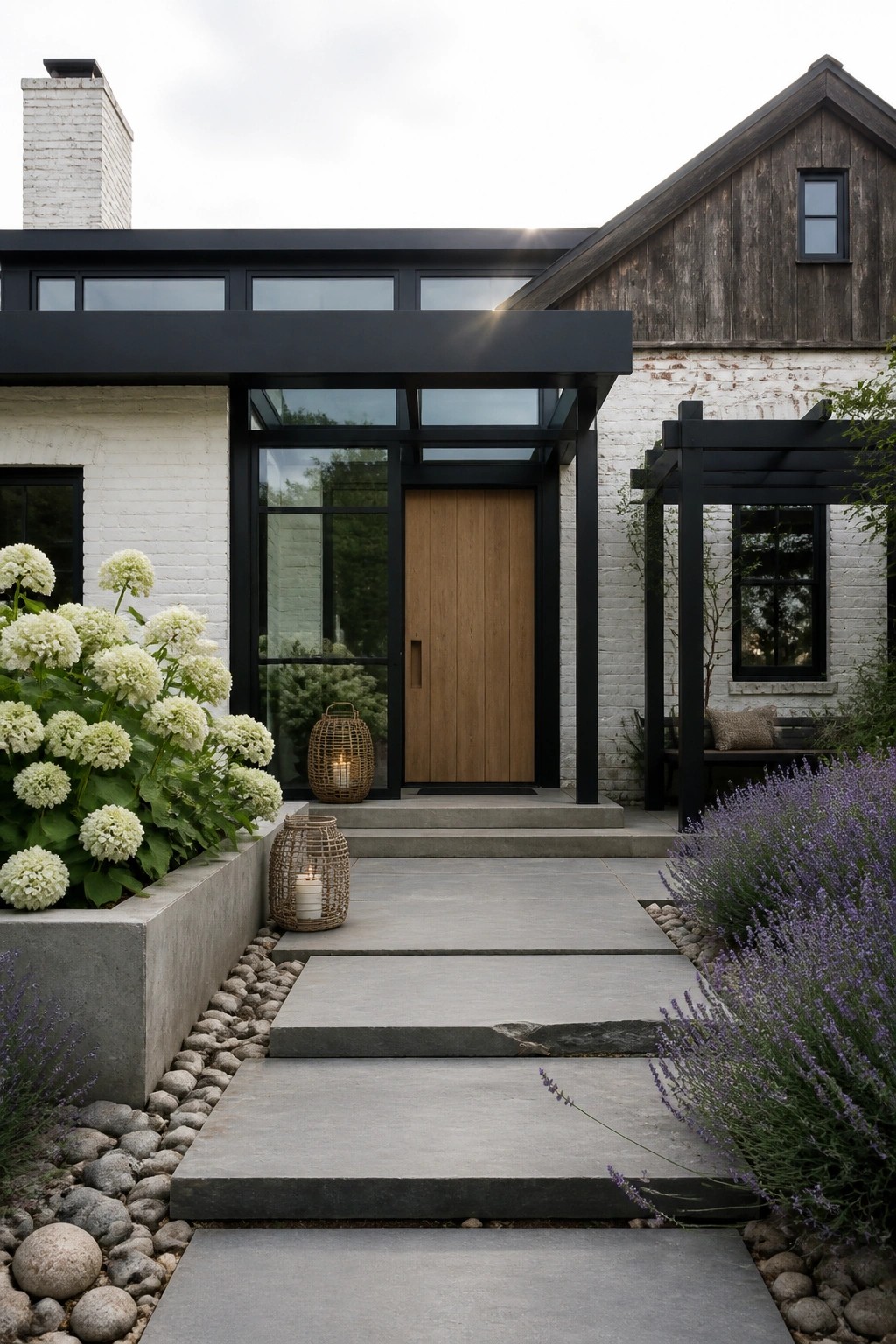 Front view of a white brick house with a wooden front door under a black-framed glass canopy and a concrete pathway lined with plants.