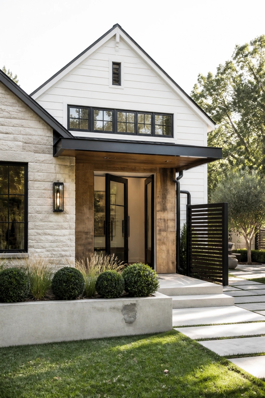 Front view of a modern farmhouse with white horizontal siding, stone veneer on the left wall, black-framed windows and doors, and a covered entry with wood accents.