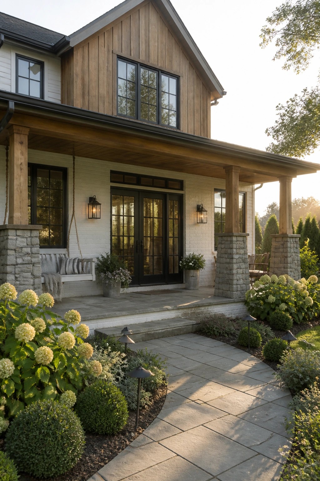 Modern farmhouse exterior showing white brick walls, a wood gable, black-framed doors and windows, and a covered porch supported by thick stone pillars.
