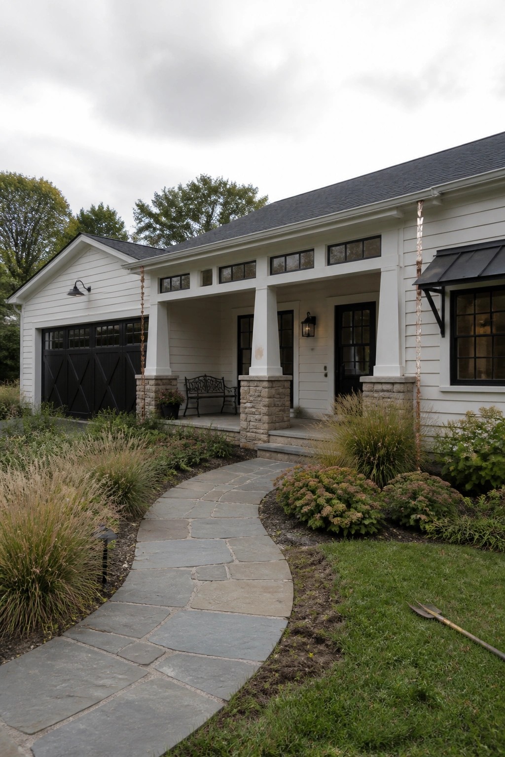 A single-story white house with black trim features a covered porch supported by white columns on stone piers, with a curving stone pathway leading to the entrance.