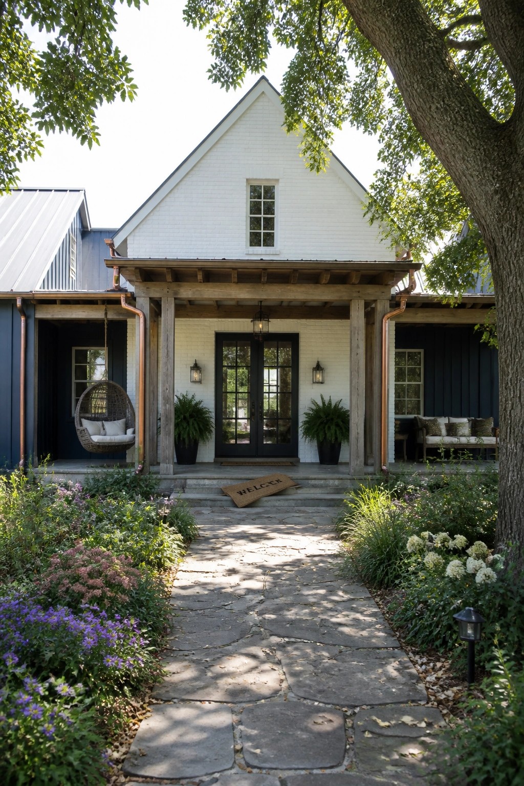 A white brick farmhouse exterior with dark blue siding, a wooden porch with black double doors, hanging chair, and a stone path leading to the front steps.