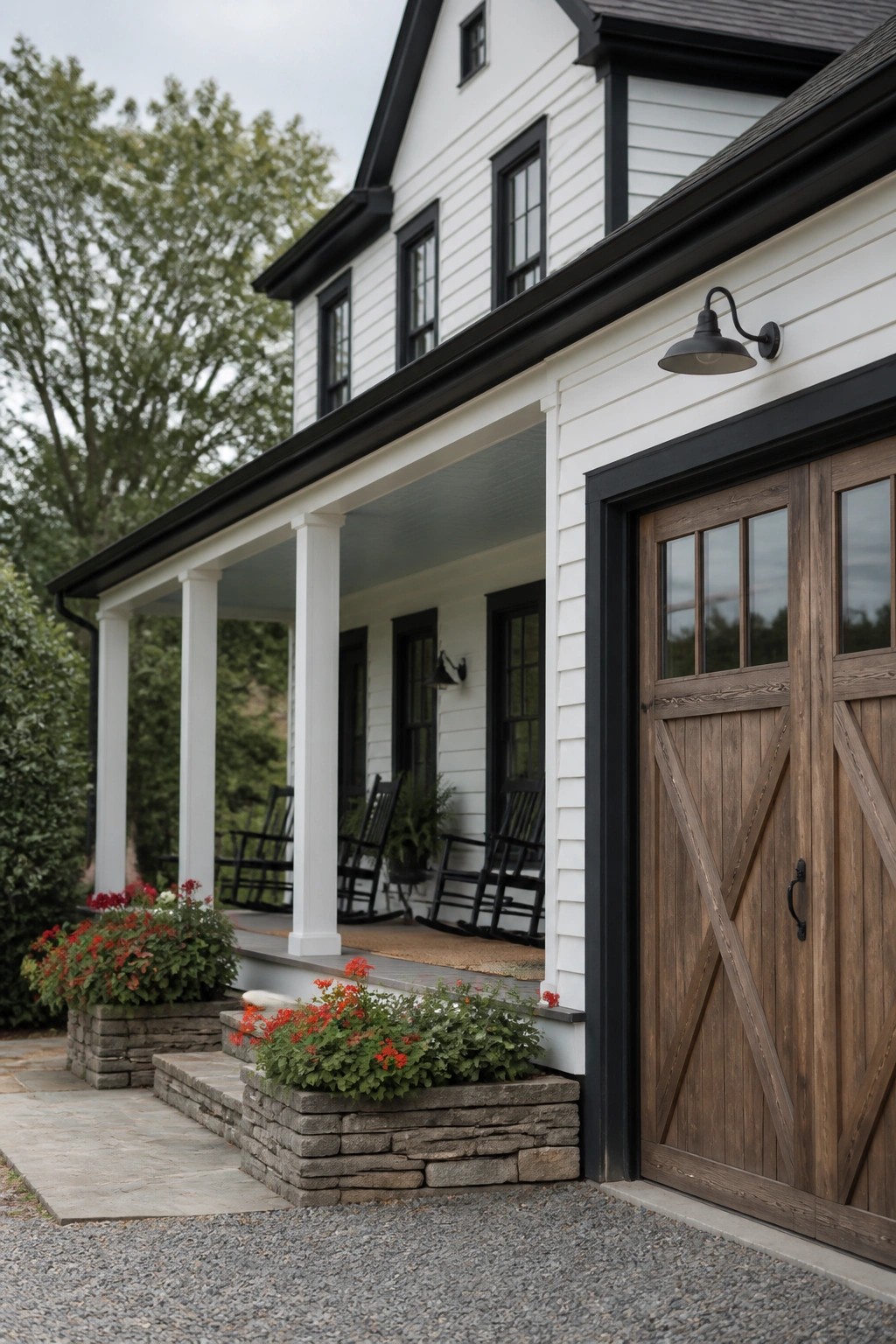 A white farmhouse exterior with black trim, a covered porch with rocking chairs, and a wooden garage door on the right.