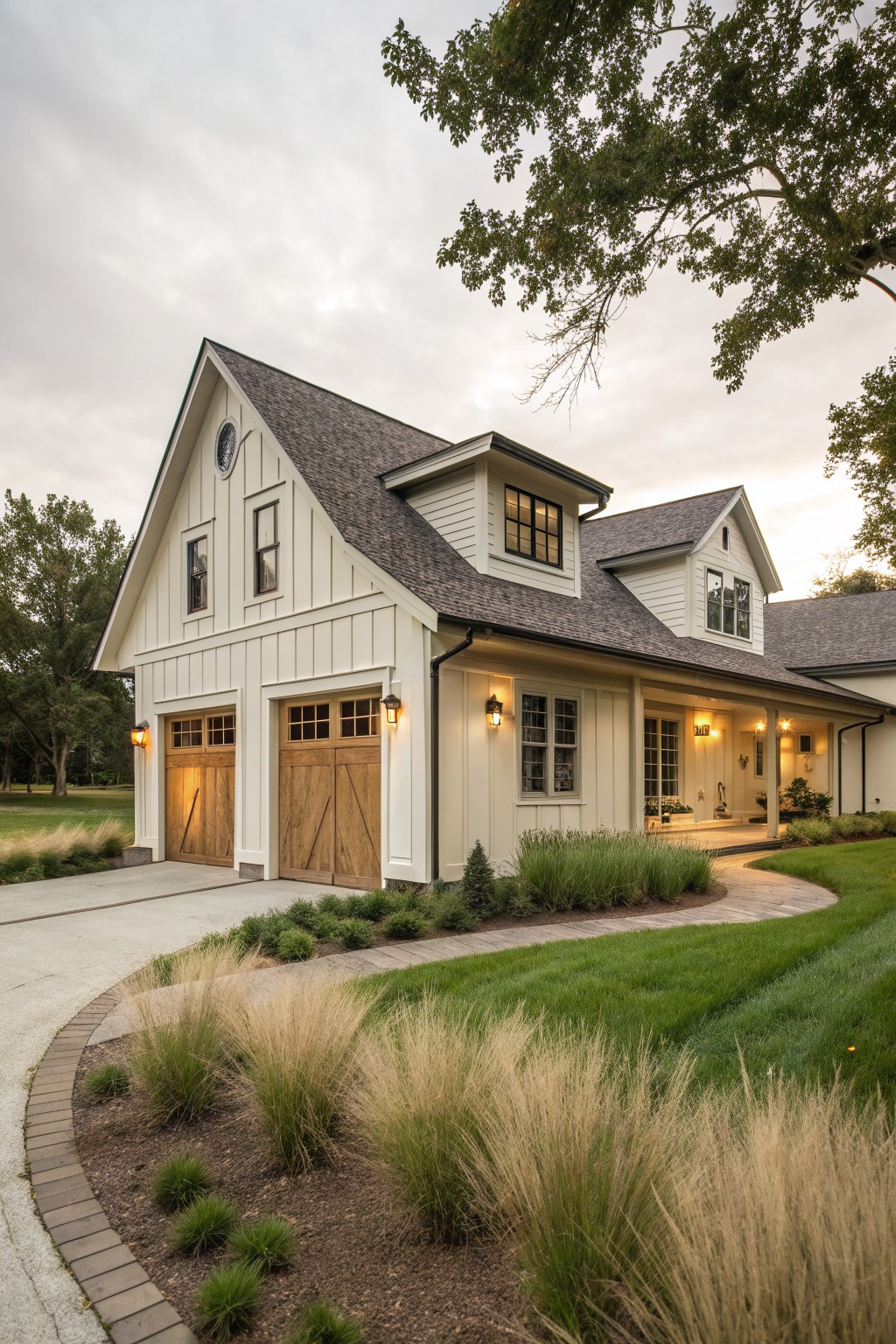 A white farmhouse exterior with two wooden barn-style garage doors, a curved driveway, and landscaping with tall grasses.