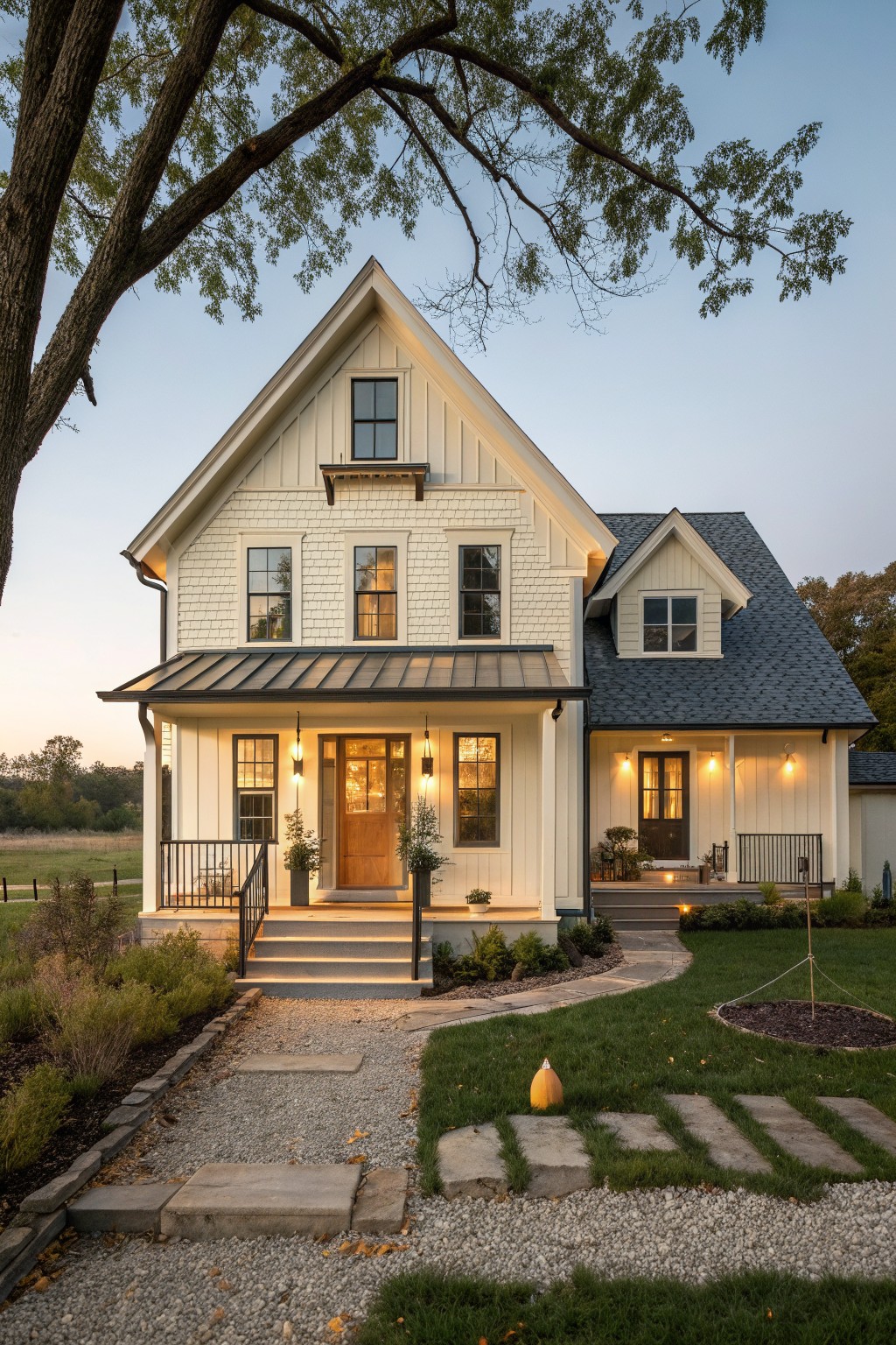 Front view of a two-story white farmhouse with a large central gable, covered porch, wooden front door, and metal porch roof at dusk.