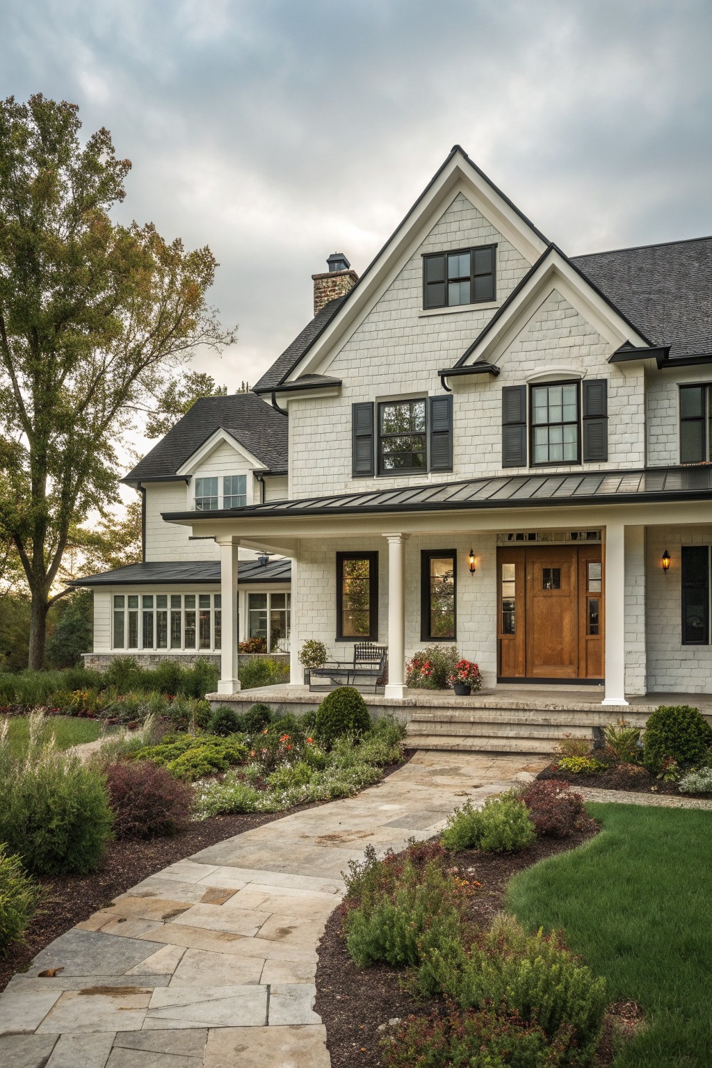 A white shingled farmhouse exterior with black shutters, a wooden front door under a porch, and a stone path leading through garden beds.