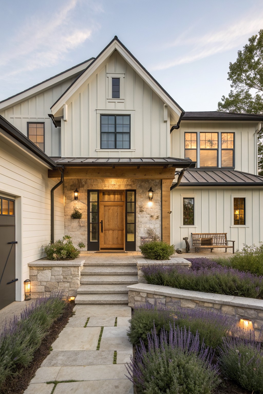 White two-story farmhouse with stone entry, wooden door, and lavender-lined pathway at dusk.
