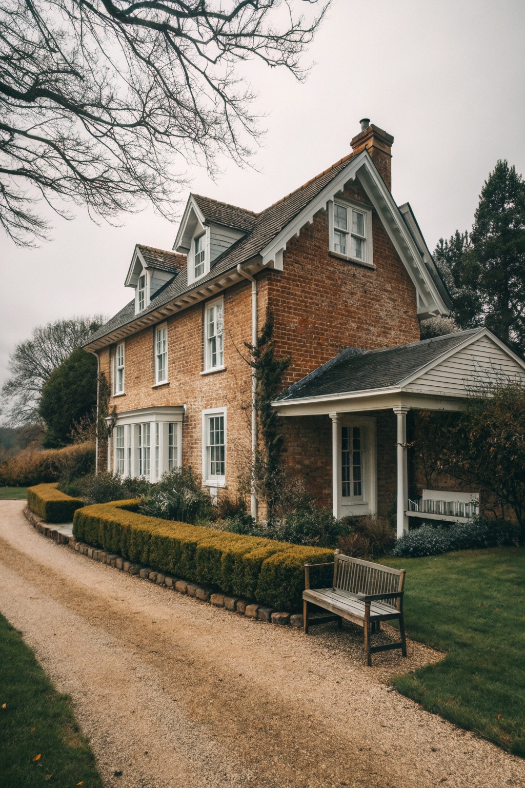 Red brick house with white windows beside gravel path and wooden bench